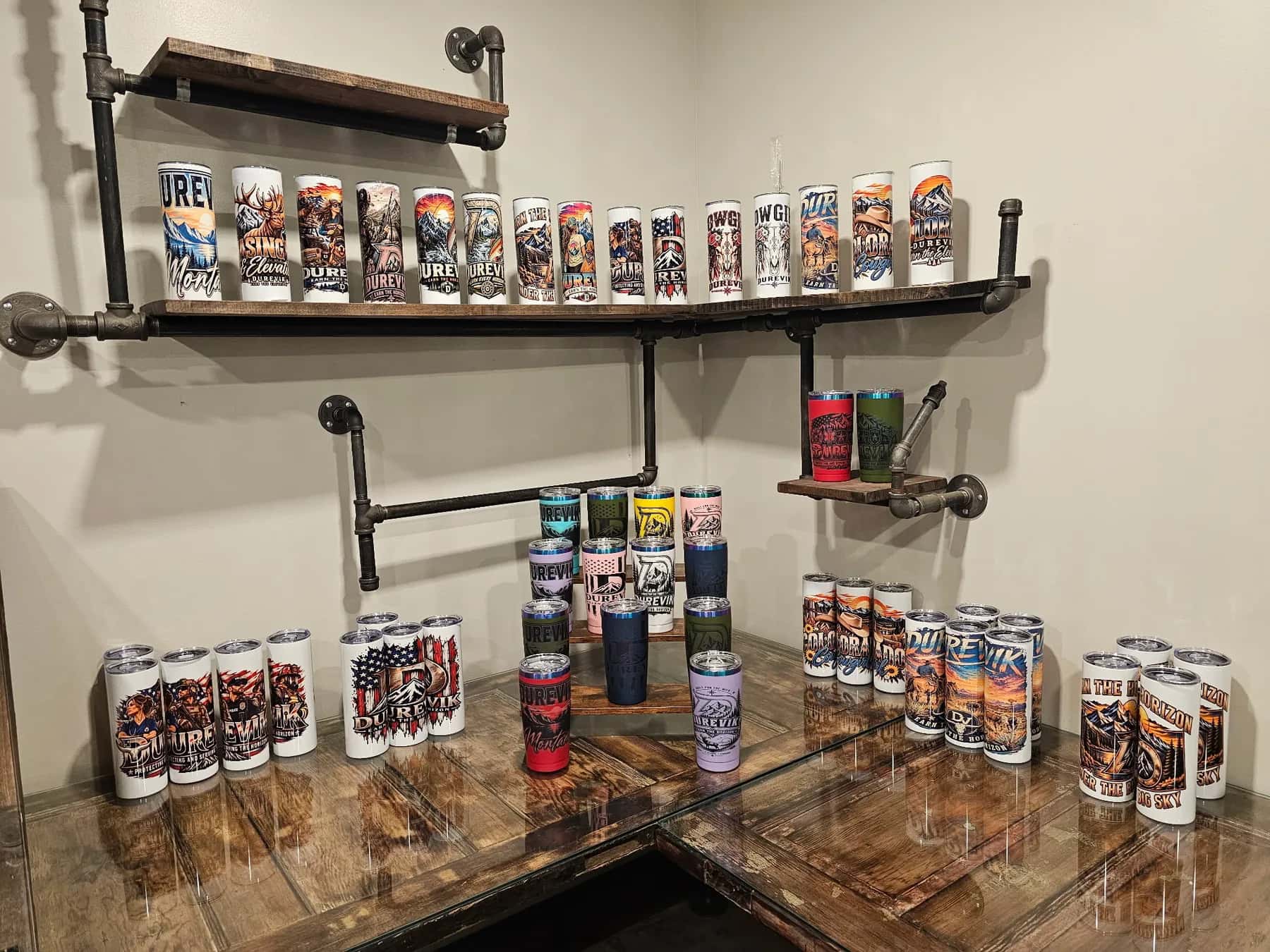 The tumbler wall in our shop: full-wrap sublimation tumblers on pipe shelves and the counter